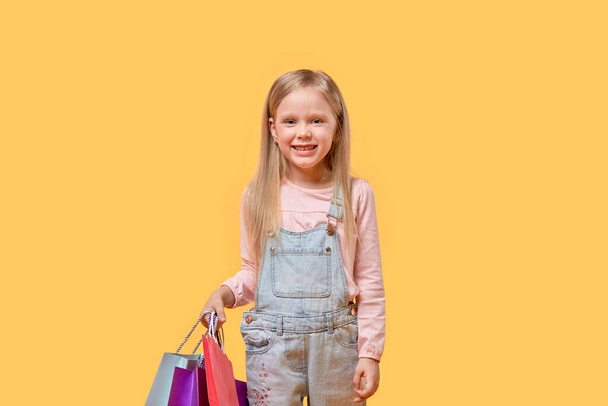 Happy blonde girl holding gifts in multi-colored bags. - Foto, imagen