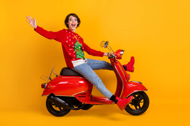 Full length profile side photo of extreme girl drive scooter fast speed x-mas noel tradition party ride wear christmas tree decor jumper sweater denim jeans isolated shine color background - 写真・画像