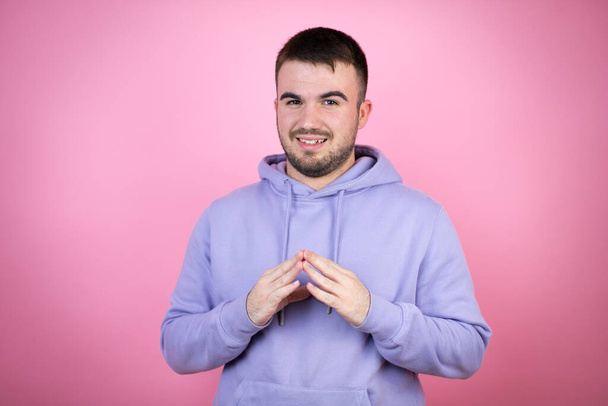 Jonge knappe man draagt casual sweatshirt over geïsoleerde roze achtergrond met handen bij elkaar en vingers gekruist glimlachend ontspannen en vrolijk. Succes en optimisme - Foto, afbeelding