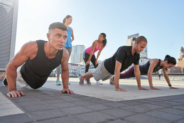 Young mixed race athletes doing push ups on city square - Photo, Image