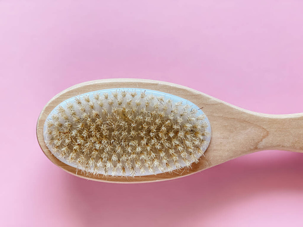 Brush with a handle for dry anti-cellulite massage or brushing in the hand of a girl in soft pink colors.  Beauty concept. - Photo, Image