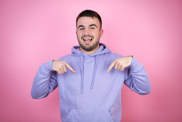 Young handsome man wearing casual sweatshirt over isolated pink background looking confident with smile on face, pointing oneself with fingers proud and happy. - Photo, Image