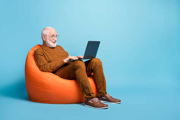 Portrait of his he nice attractive focused bearded grey-haired man sitting in bag chair using laptop writing email letter browsing web wi-fi isolated over blue pastel color background - Photo, Image