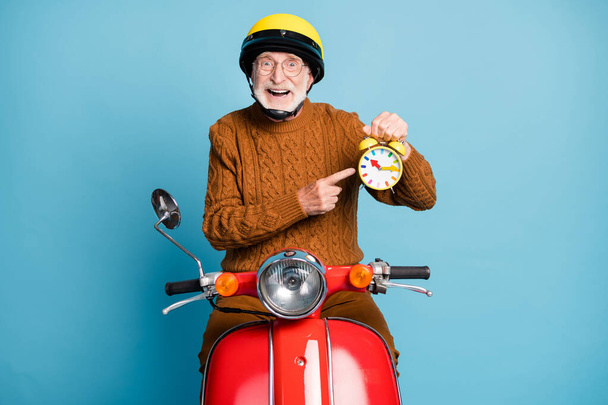 Portrait of his he nice attractive funky cheerful cheery glad bearded grey-haired man riding moped holding in hand clock hurry rush punctuality isolated over blue pastel color background - Foto, Imagem