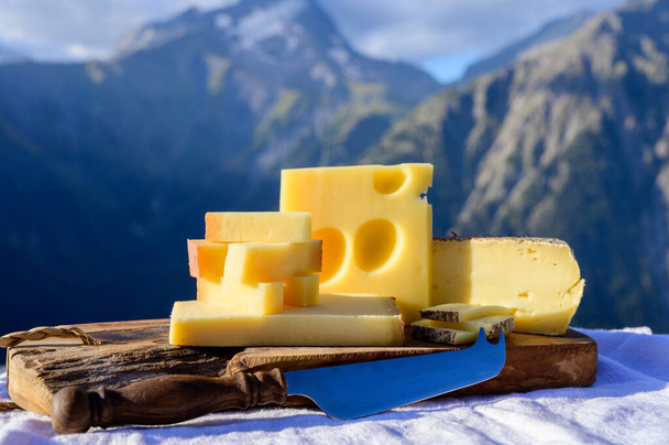 Cheese collection, French beaufort, abondance, emmental, tomme de savoie cheeses served outdoor in Savoy region, with Alpine mountains peaks in summer on background - Photo, Image