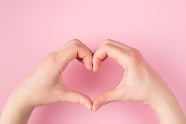 Love and romance concept. Top above overhead pov first person close up view photo of female hands making heart shape isolated on pink pastel background with copyspce - Zdjęcie, obraz