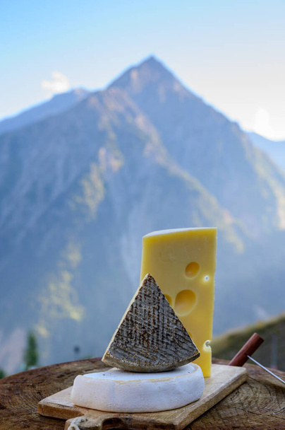 Cheese collection, French emmental, tomme and reblochon de savoie cheeses served outdoor in Savoy region, with Alpine mountains peaks in summer on background - Photo, Image