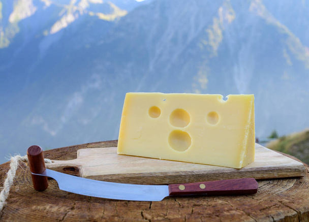 チーズコレクション、フランスのメンタル・ド・サヴォワチーズ、丸い穴の開いたサヴォイ地方の屋外で提供され、夏にはアルパイン山のピークが背景にあります。 - 写真・画像