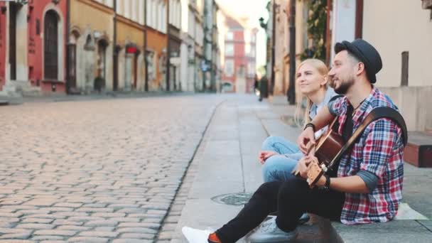 Туристы сидят на тротуаре, играют на гитаре и отдыхают - Кадры, видео