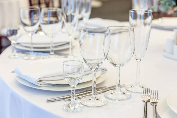 Fancy stůl set for dinner with ubkin glasses in restaurant, luxury interior background. Svatební elegantní hostina dekorace a položky pro potraviny uspořádané catering servis na bílém stolním ubrusu - Fotografie, Obrázek