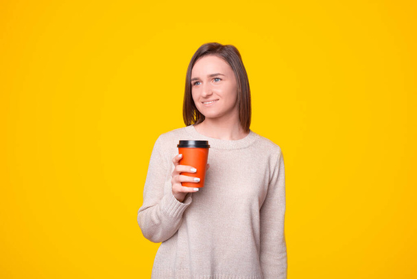 Portré fiatal nő áll a sárga háttér és ivás csésze kávét menni - Fotó, kép