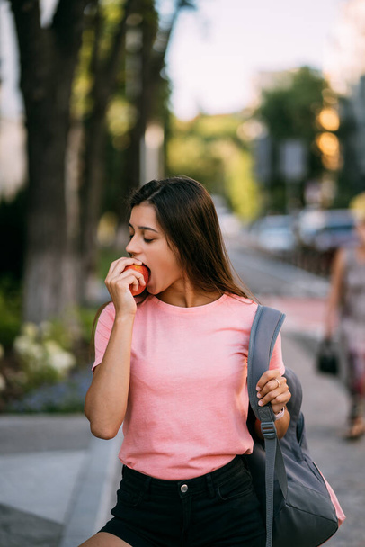 Giovane donna mordere mela contro uno sfondo stradale - Foto, immagini