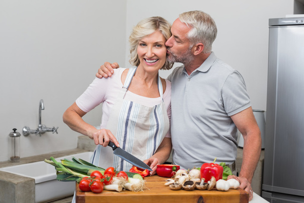 Man kissing woman as she chops vegetables in kitchen - Fotó, kép
