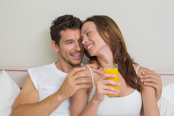 Happy relaxed couple with orange juice in bed - Фото, зображення