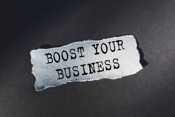 BOOST YOUR BUSINESS - text on torn paper on dark desk in sunlight. - Zdjęcie, obraz