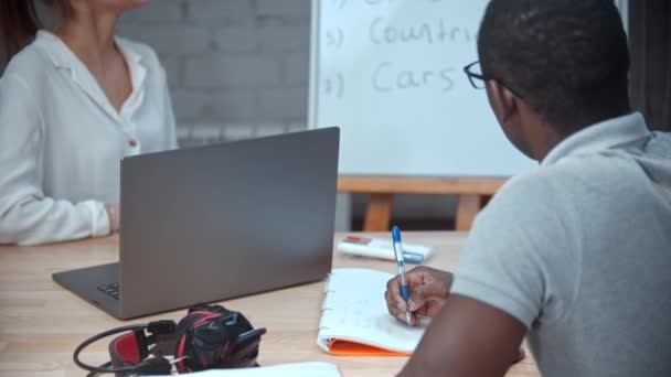 Une enseignante donne une leçon d'anglais à un homme noir - pointant du doigt le tableau avec des thèmes pour la première leçon - Séquence, vidéo