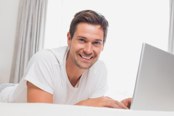 Portrait of relaxed casual man using laptop in bed - Zdjęcie, obraz