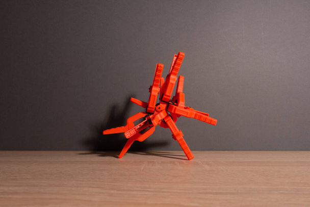 Clothespins, carpentry clamps of orange color lie on a wooden table. A pyramid in the form of a robot made of clamps. - Photo, Image