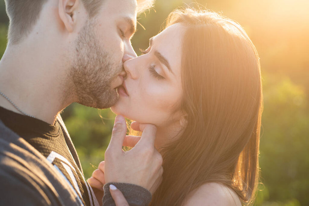 Close-up of young romantic couple is kissing. Profile of beautiful people in love expressing and affection while kiss each other with closed eyes on autumn sunset. - Фото, зображення
