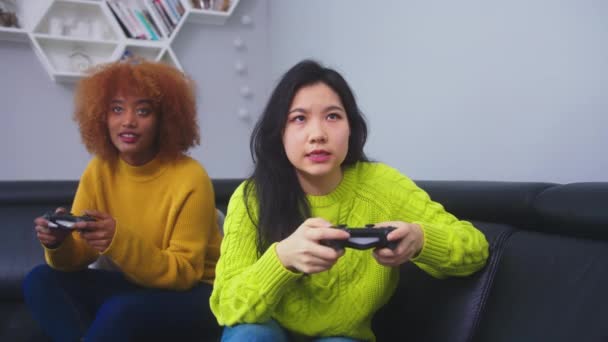 Összpontosított versenyképes leszbikus pár játék otthon, ázsiai és afro-amerikai nők, amelyek vicces boldog pillanat együtt kanapén a nappaliban éjszaka. - Felvétel, videó