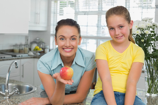 Mulher mostrando maçã por filha na cozinha
 - Foto, Imagem