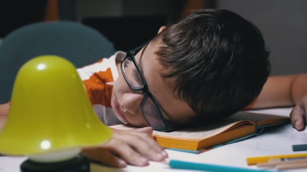 Το περίεργο αγόρι με τα γυαλιά κοιμάται στο βιβλίο διαβασμένο στο τραπέζι. Κόπωση, ύπνος - Πλάνα, βίντεο