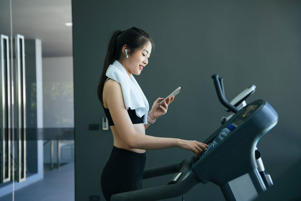 Gezonde aziatische vrouw selecteren streaming song op smartphone tijdens het trainen op loopband machine. - Foto, afbeelding