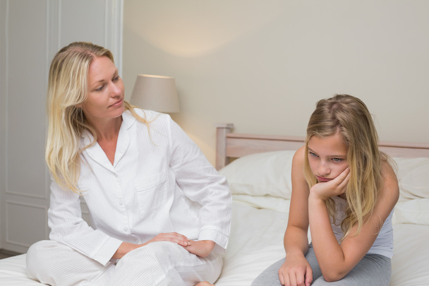 Woman looking at sad girl sitting on bed - Photo, image