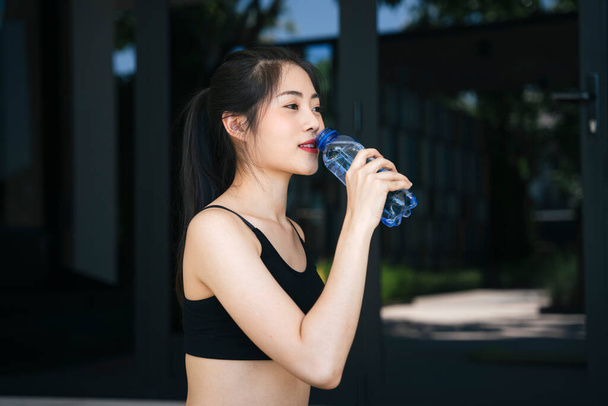 健康的なアジアの女性はジムでボトルから休憩飲料水を取ります. - 写真・画像