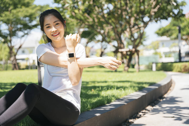 Deportiva asiática mujer estirando los brazos caliente antes de trotar en parque. - Foto, imagen