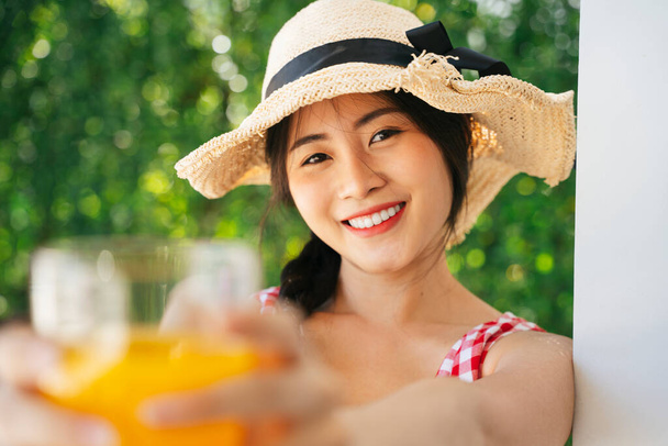 美しいアジアの女性の肖像帽子は屋外で新鮮なオレンジジュースを楽しむ. - 写真・画像