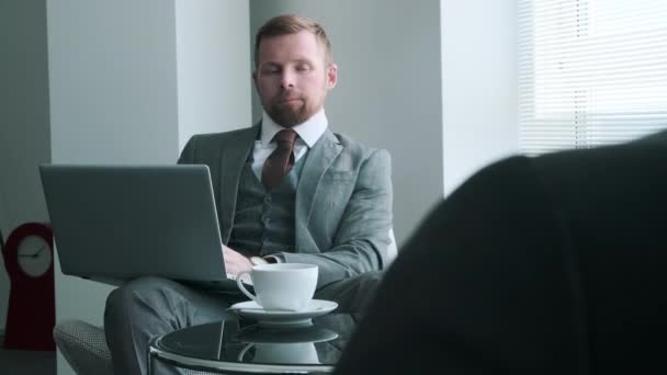 Über-die-Schulter-Aufnahme eines gutaussehenden kaukasischen Geschäftsmannes im grauen Anzug, der vor seinem Kollegen sitzt, der am Laptop arbeitet und etwas diskutiert - Filmmaterial, Video