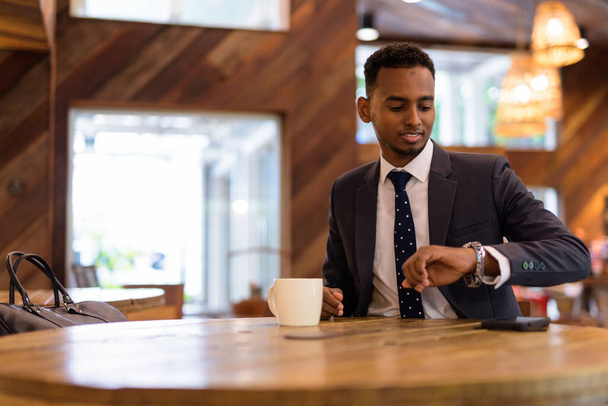 Бізнесмен сидить і перевіряє час зі свого годинника в кав'ярні
 - Фото, зображення