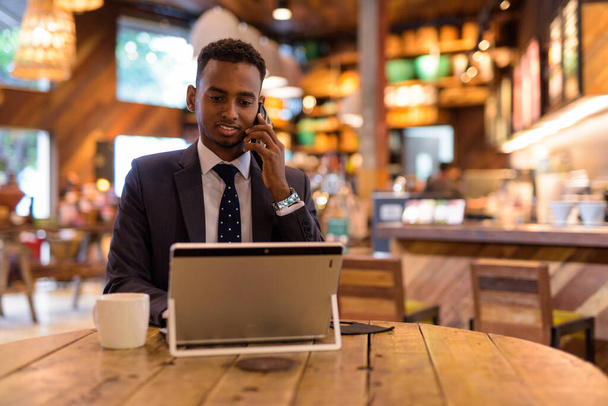 Businessman using laptop computer and talking at phone at coffee shop - Fotó, kép