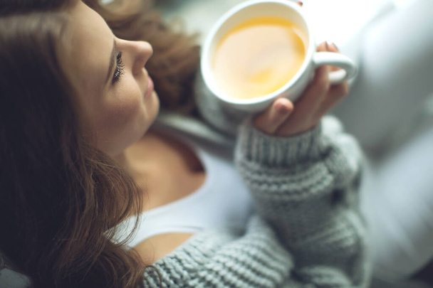 Detailní záběr ženských rukou s džbánem nápoje. Krásná dívka v šedém svetru drží šálek čaje nebo kávy v ranním slunci. Hrnek pro váš design.  - Fotografie, Obrázek