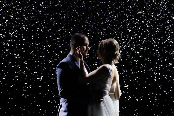 Tierna pareja enamorada en el fondo de la nieve que cae. Un hombre con un traje y una mujer encantadora con un vestido blanco se tocan las caras. De cerca.. - Foto, Imagen