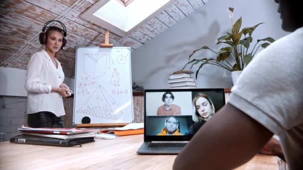 Una lección de matemáticas en línea - mujer de pie junto al tablero y sus estudiantes en la pantalla de la computadora portátil escuchándola - Imágenes, Vídeo
