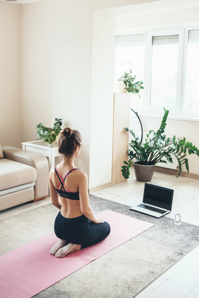 Donna sportiva caucasica in abbigliamento sportivo sta guardando il computer portatile sul pavimento durante la lezione di yoga online - Foto, immagini