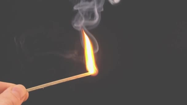 Valaistu tulitikku palaa savun kanssa harmaalla taustalla. Käsite hidastettu video tulella. Käsi sytyttää tulitikun.. - Materiaali, video