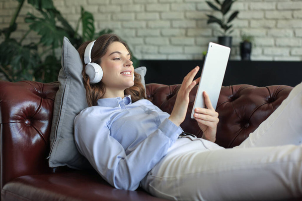 Smiling young woman with headphones and digital tablet on the sofa - Foto, Imagen