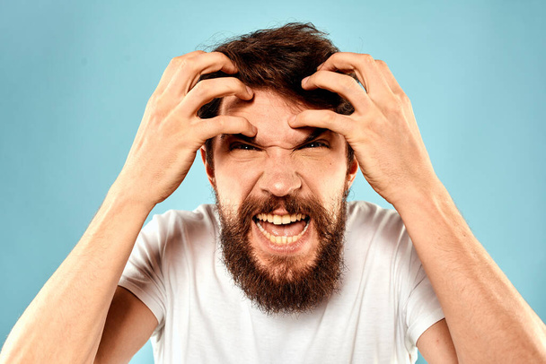 Bearded man in white T-shirt emotions gestures with hands displeased facial expression blue background - Photo, Image