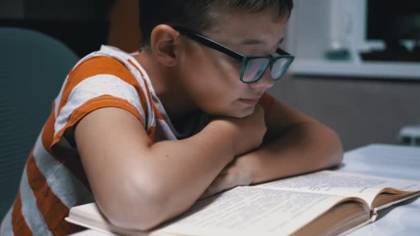 Neugierig liest ein ernsthafter Junge mit Brille zu Hause ein interessantes Buch - Filmmaterial, Video
