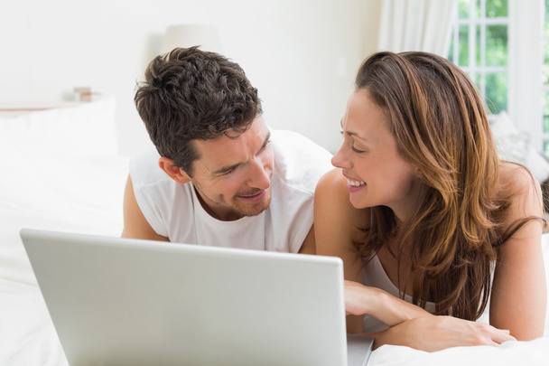 Smiling couple using laptop in bed - Foto, imagen