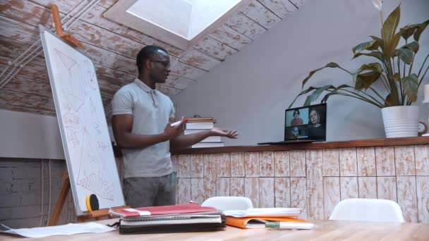 Çevrimiçi matematik dersi. Gözlüklü Afro-Amerikan bir öğretmen kurulun yanında duruyor ve öğrencilerine bilgisayar ekranındaki materyalleri anlatıyor. - Video, Çekim