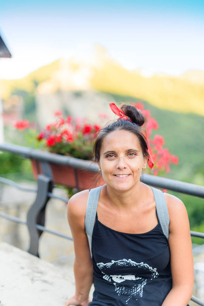 Portret van mooie vrouw met gebonden haar en shirt met rode bloemen en bergachtig landschap op de achtergrond (selectieve focus). Castelmezzano, Italië. - Foto, afbeelding
