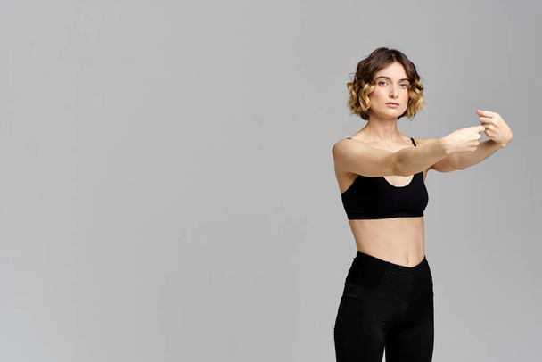 Una donna snella in leggings neri su uno sfondo grigio gesti con le mani ginnastica sport - Foto, immagini