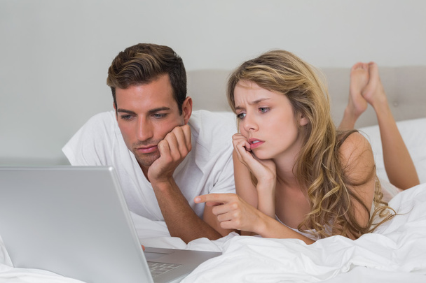 Couple using laptop in bed at home - 写真・画像