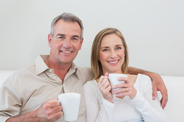 Relaxed loving couple with coffee cups in living room - Zdjęcie, obraz