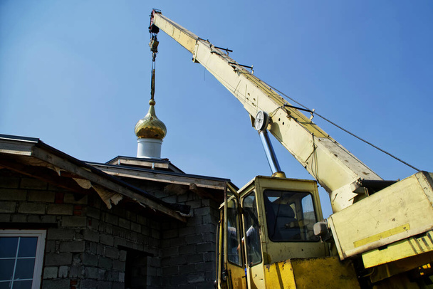 Montage der Kuppel auf dem Dach einer im Bau befindlichen Kirche mit einem Kran. Blauer Himmel. Religion und Symbole - Foto, Bild