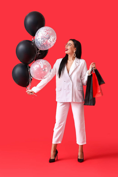 Piękna młoda kobieta z torbami na zakupy i balonami na tle koloru. Wyprzedaż Black Friday - Zdjęcie, obraz